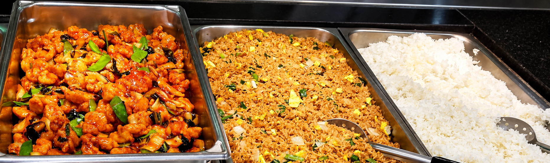 Hot buffet line with orange chicken, fried rice, and steamed white rice in stainless steel trays